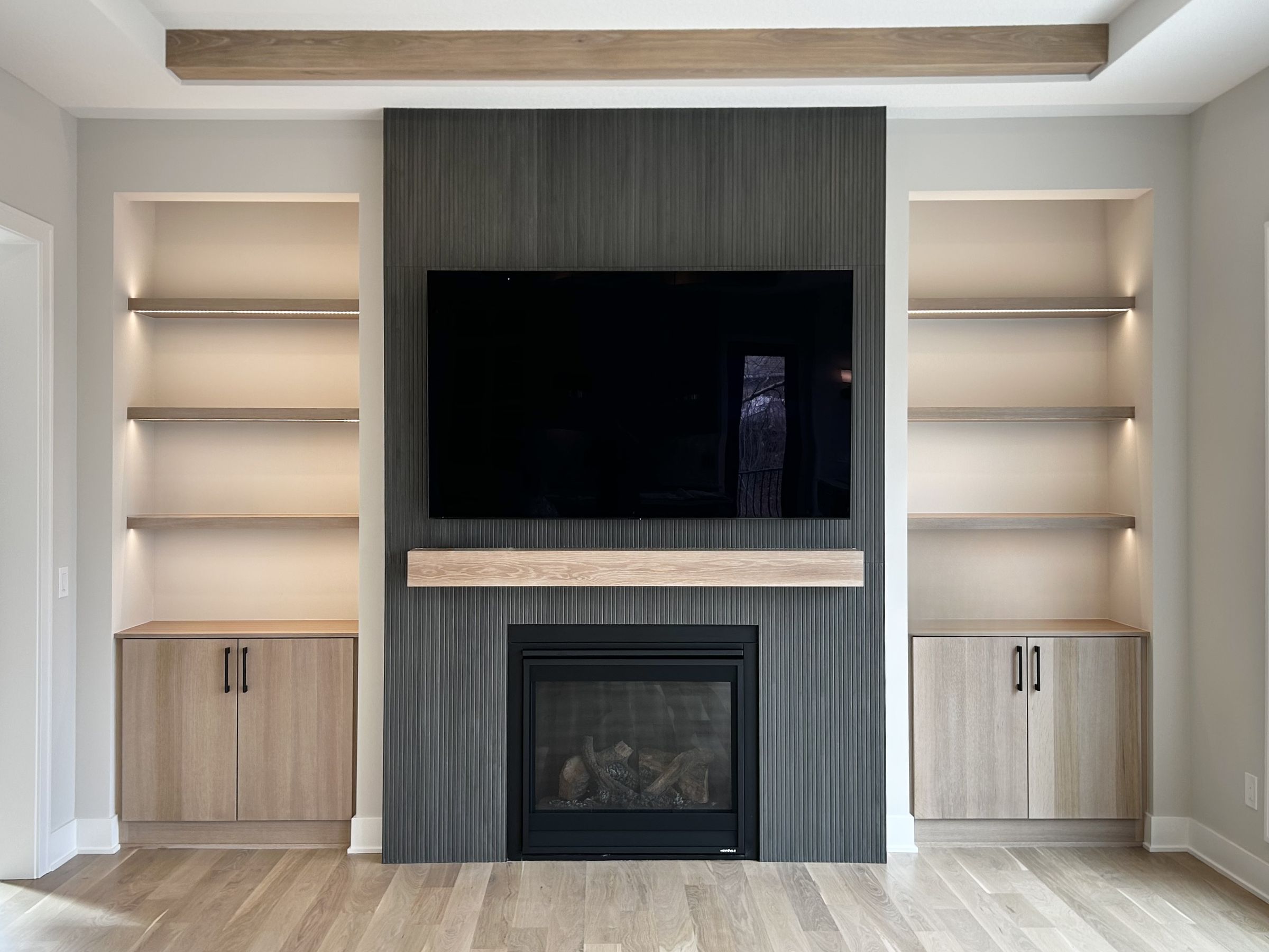 Birchpond living room with a dark fluted fireplace wall, a white oak mantel, and lit floating shelves above white oak cabinets on either side